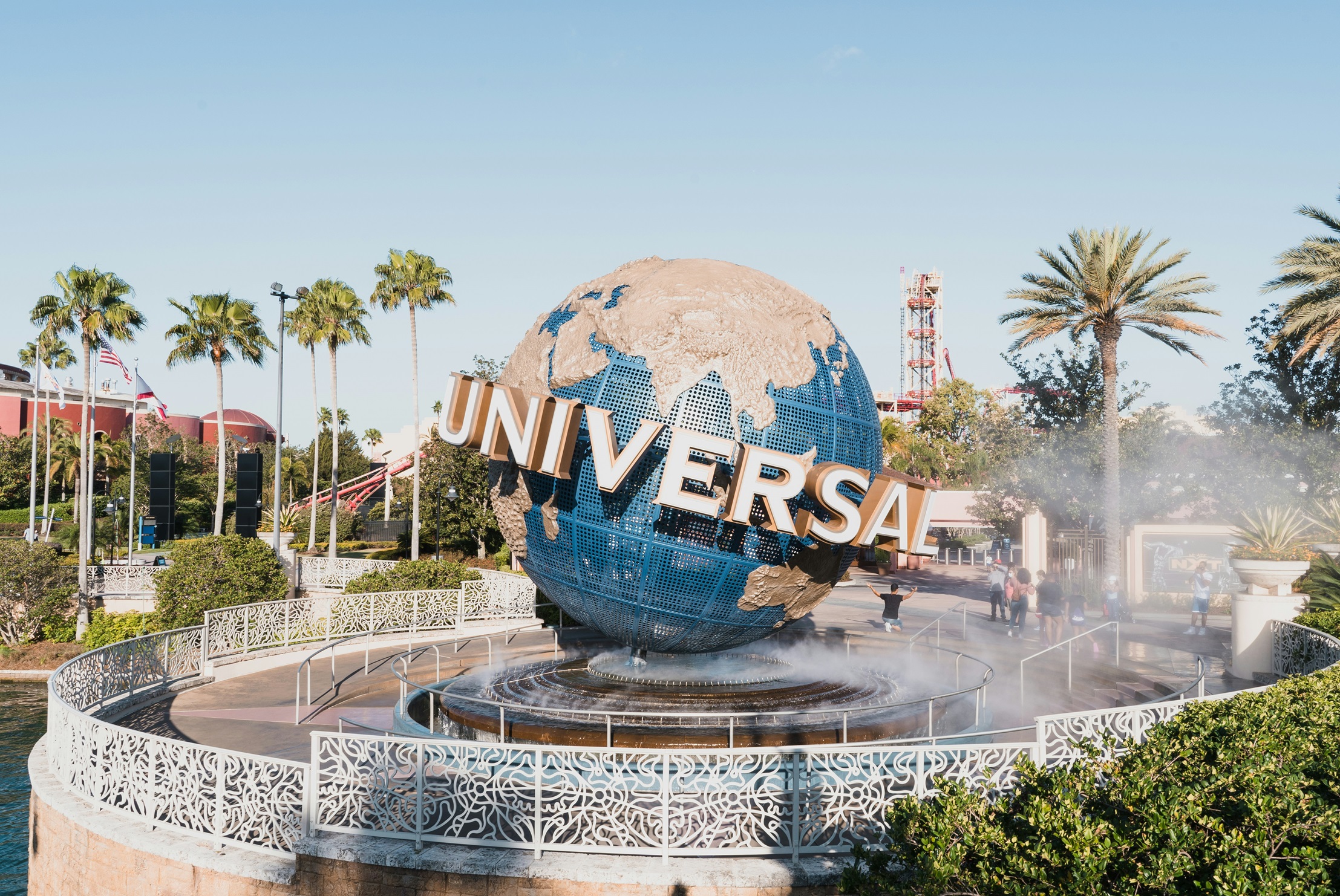 A large globe with the word "Universal" in front of it at Universal Studios, surrounded by palm trees and mist from fountains
