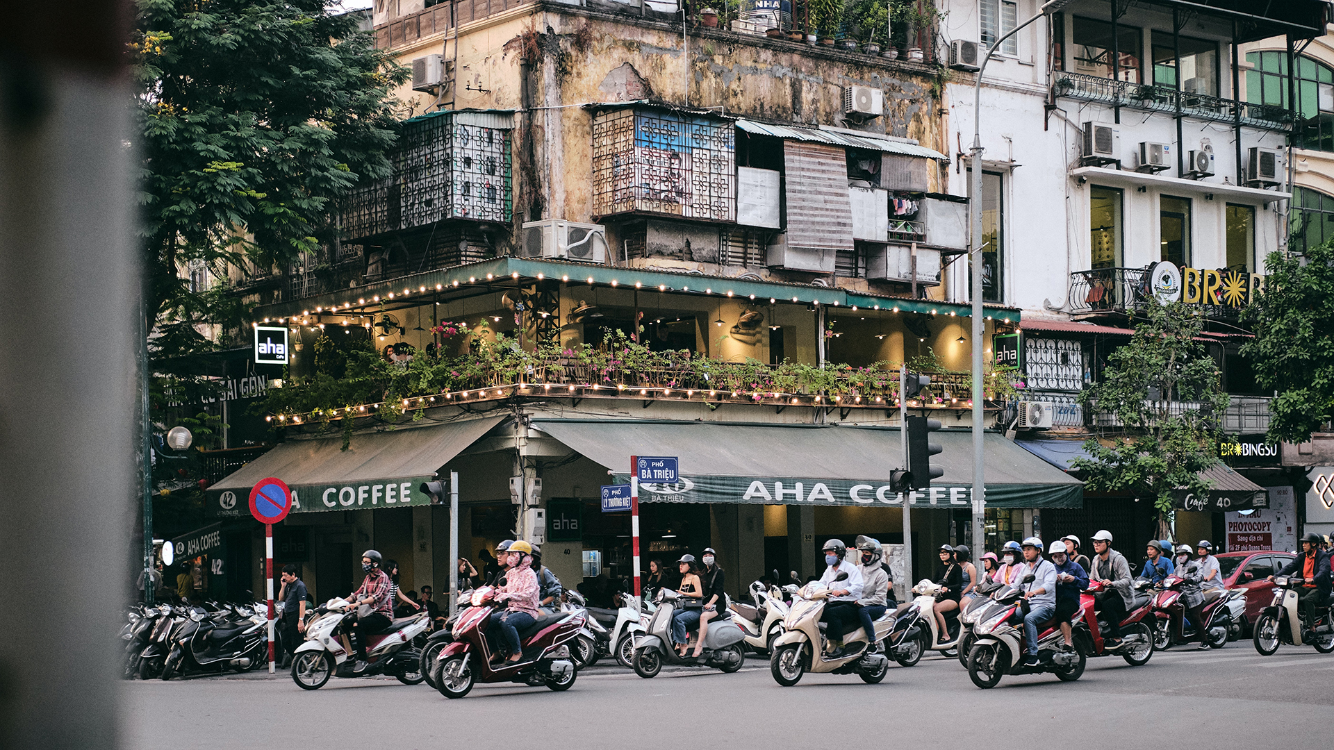 A busy road with people riding motorcycles with a coffee shop on the corner