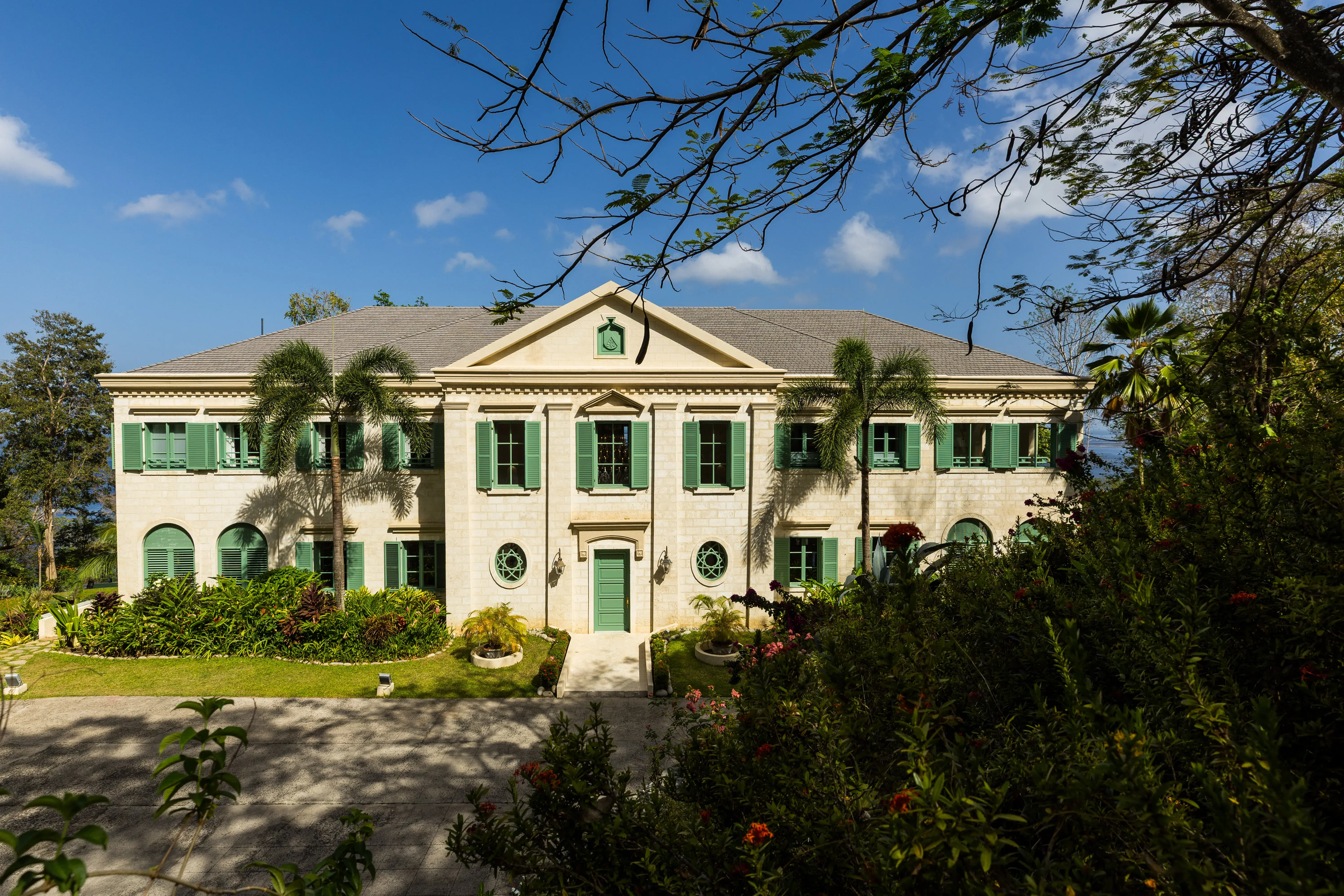 Front exterior view of La Belle Helene luxury villa in St Lucia, featuring elegant green shutters and tropical landscaping under a bright blue sky.