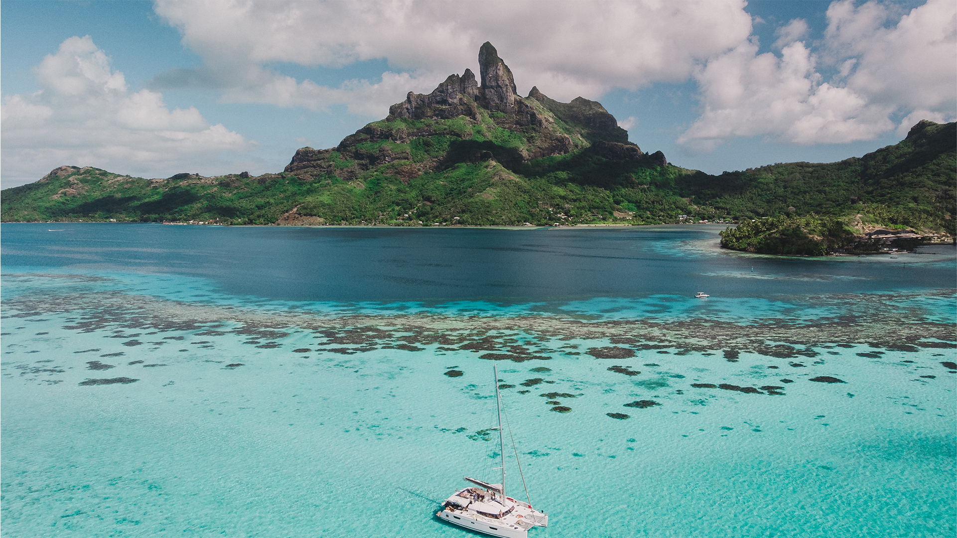 Aerial view of a catamaran on clear turquoise waters near a lush green mountainous island.