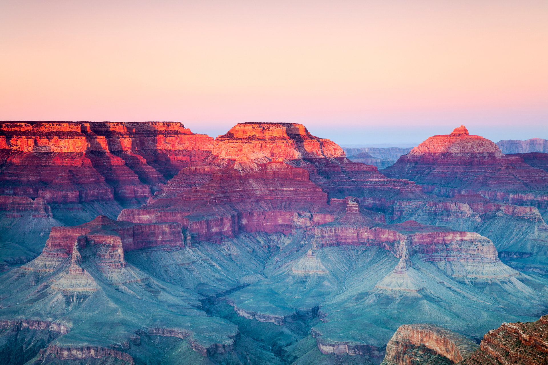 A view of the Grand Canyon at sunset, with the sun casting a glow over the rugged terrain and deep valleys below.