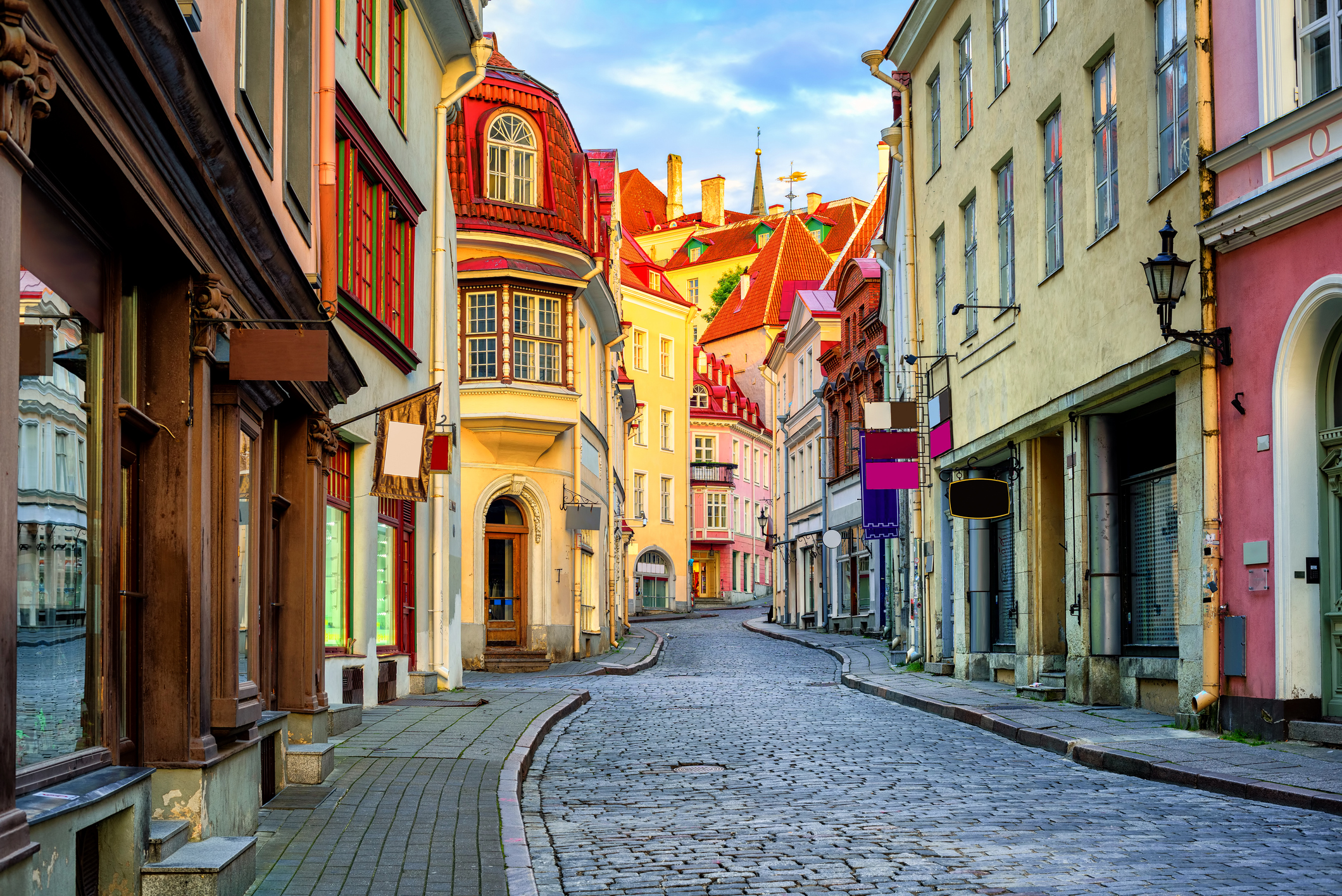 A cobblestone street winds through a picturesque European old town with colourful, historic buildings under a clear blue sky.