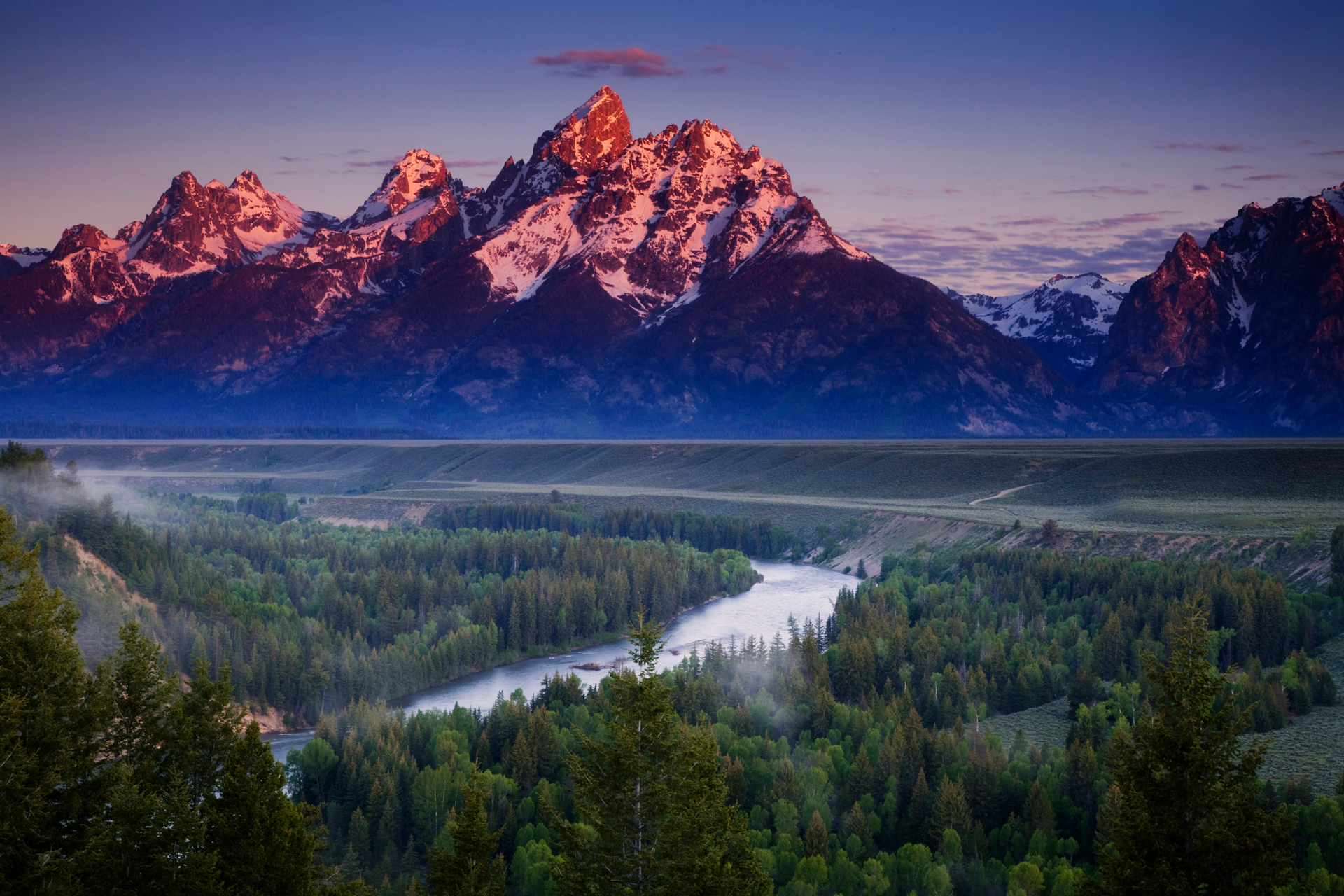 A view of the Grand Teton mountains in the morning as the mountains catch some alpen glow and the Snake River shimmers