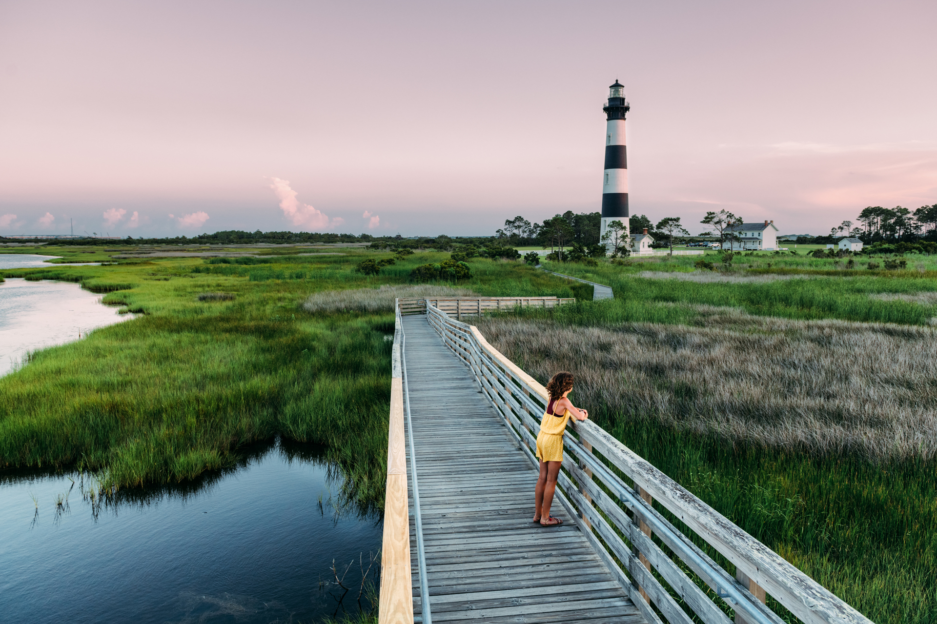 A woman wearing yellow stood on a wooden walkway nearby a red and white lighthouse