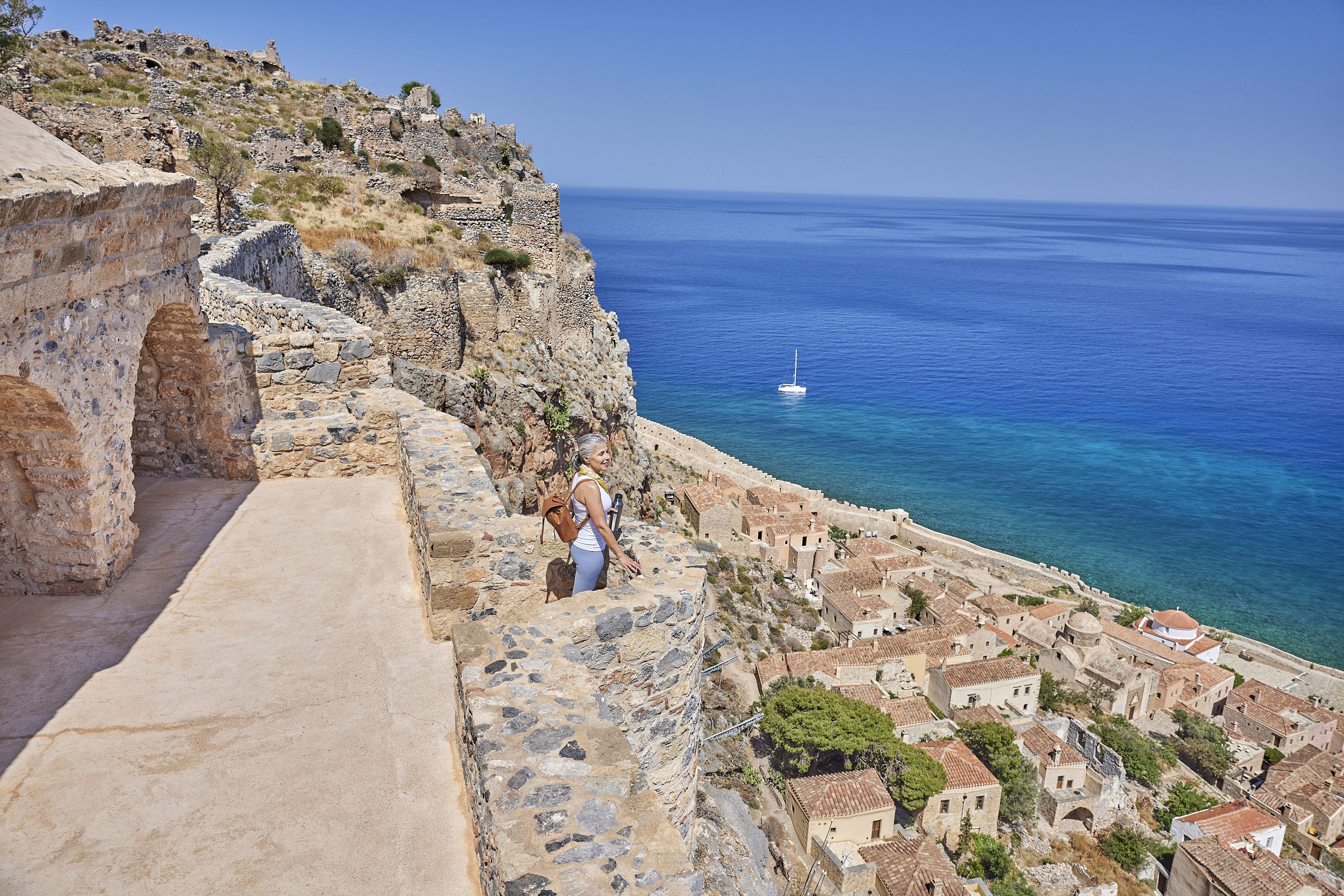 A woman standing on a stone veranda overlooking a coastal town with the sea beyond