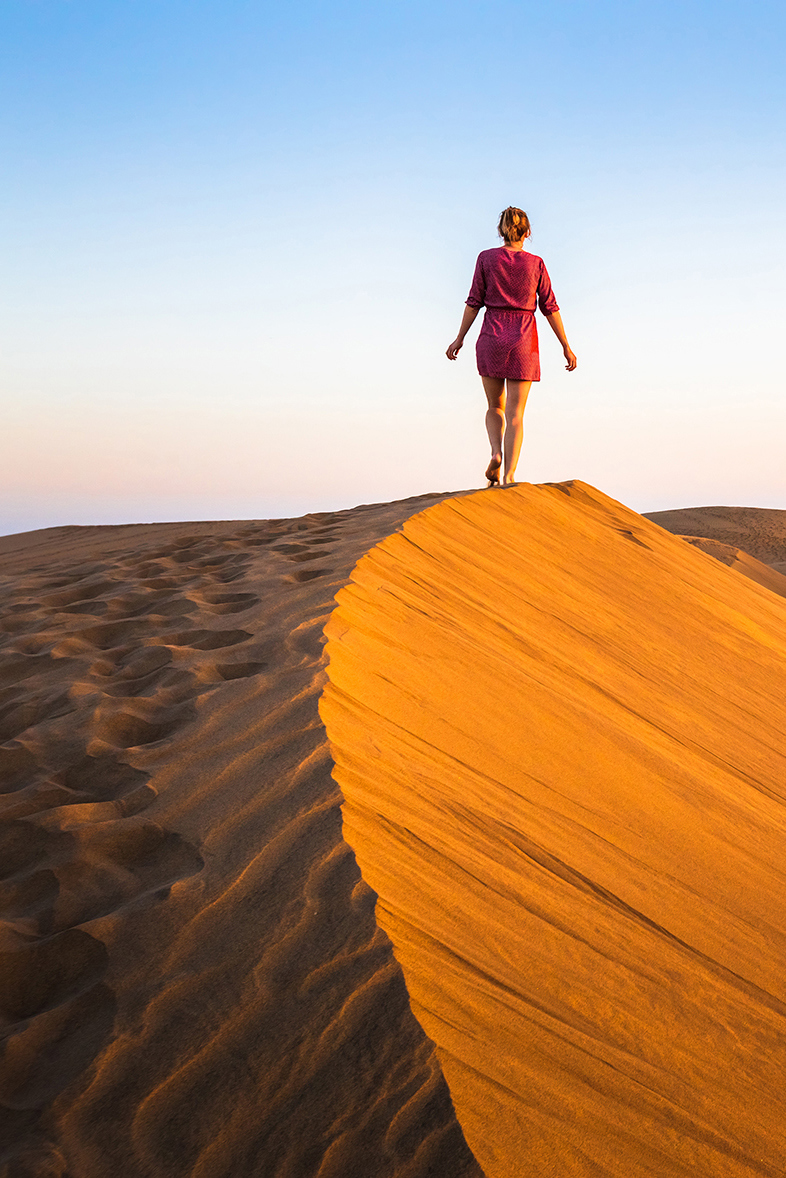 Woman in red outfit walking along the sand dunes in Oman