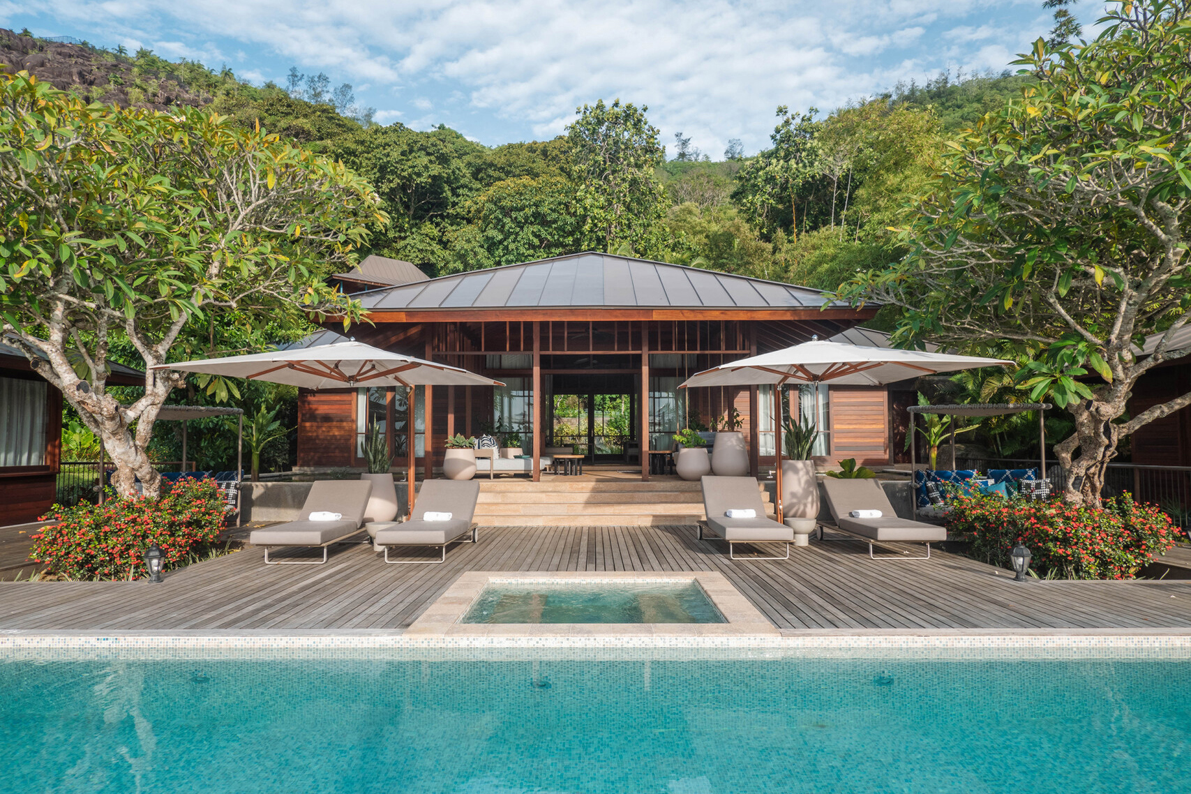 Villa surrounded by green trees with sun loungers and umbrellas by the private pool