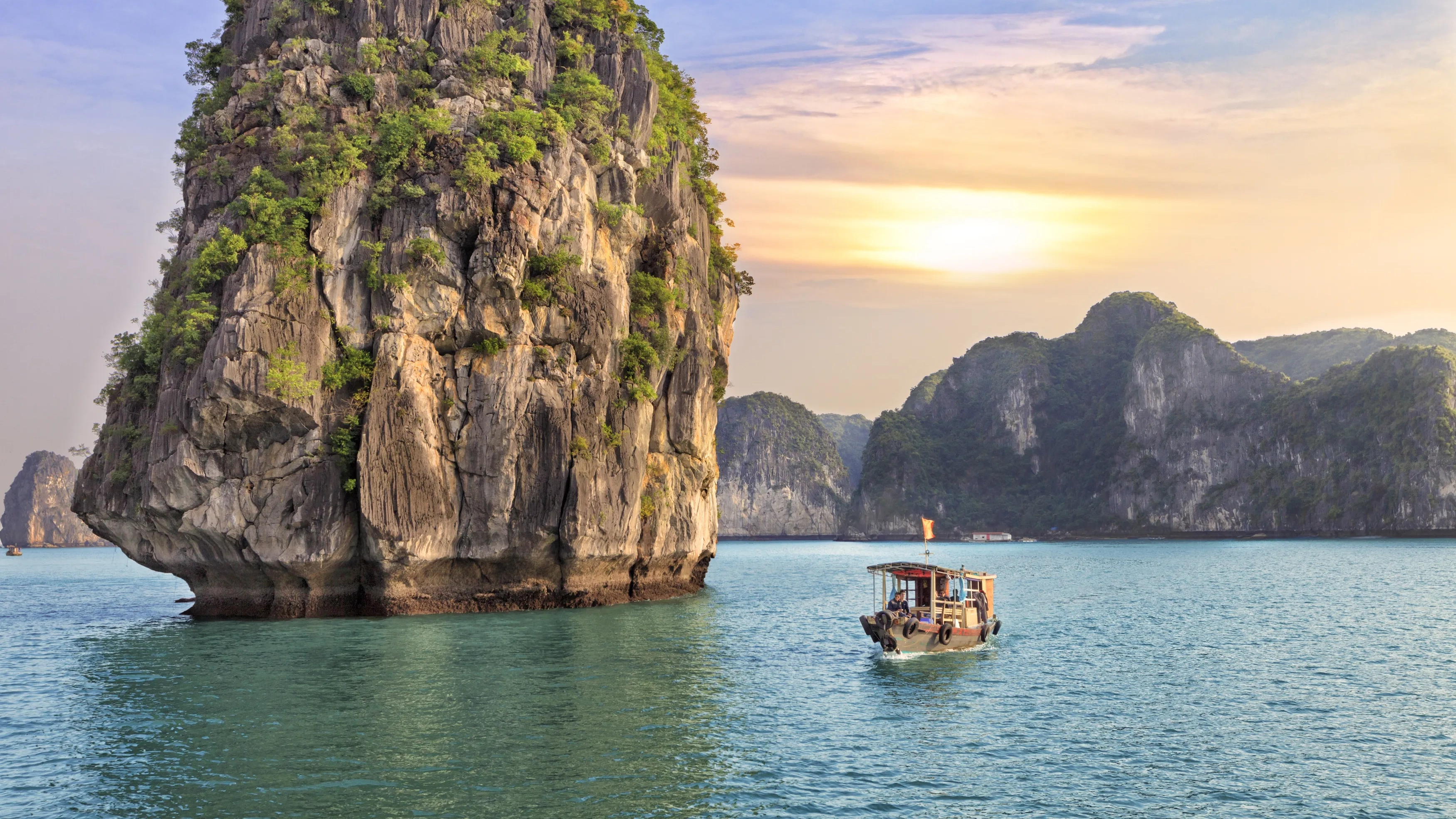 A traditional Vietnamese junk sailing between the limestone rocks of Halong Bay at sunset