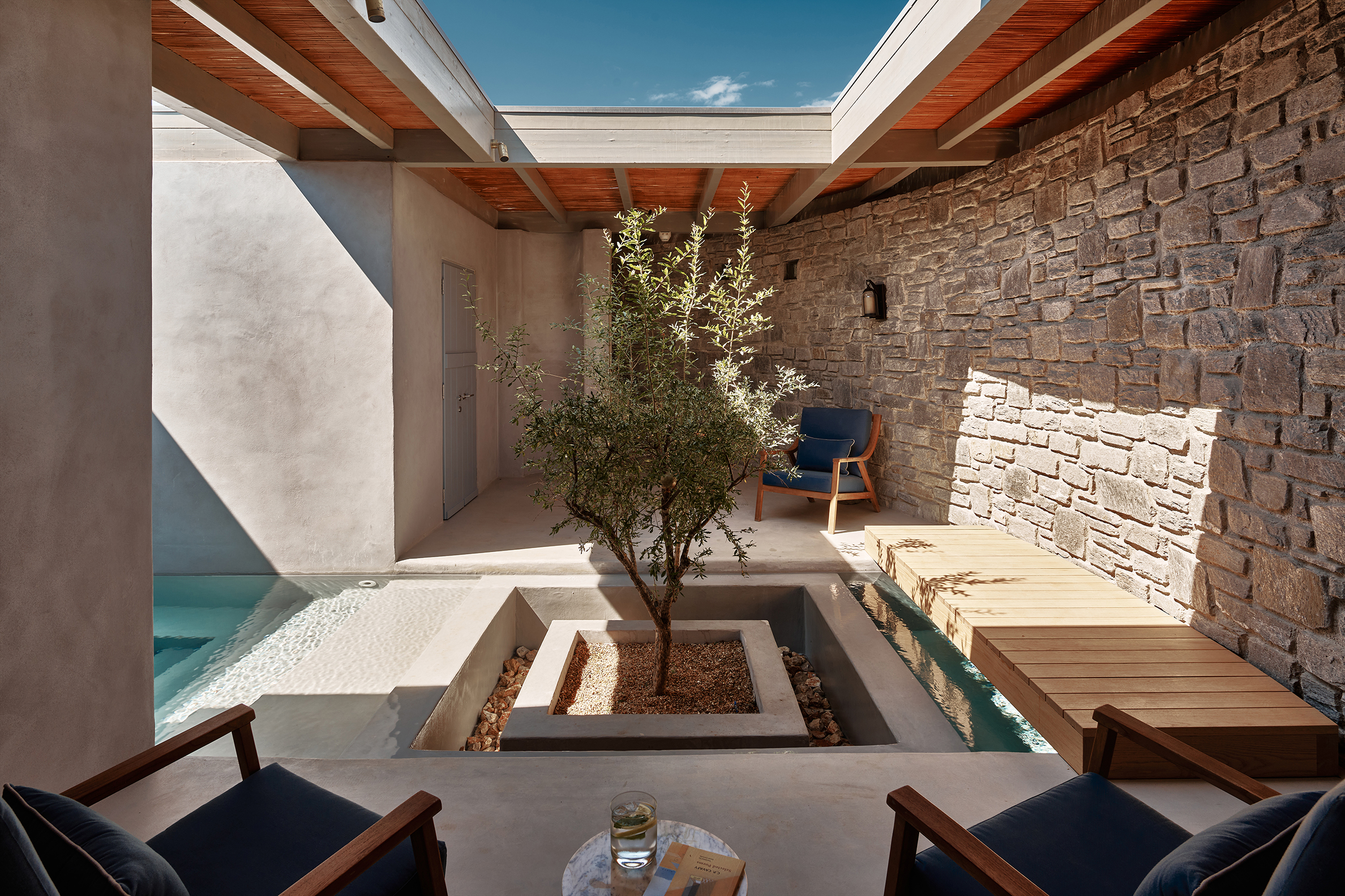A small shaded spa courtyard at Cosme with an olive tree at its centre and chairs placed around it