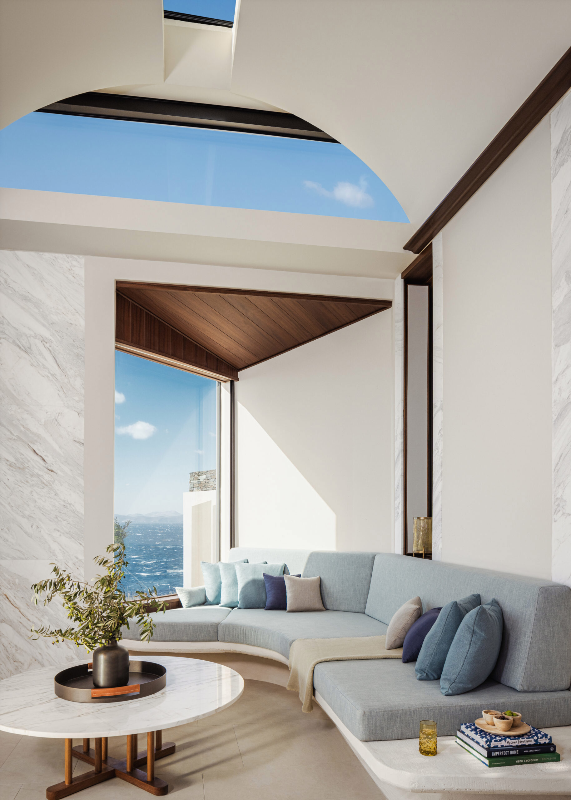 Villa lounge with cushioned blue sofa, coffee table and arched ceiling with floor-to-ceiling window