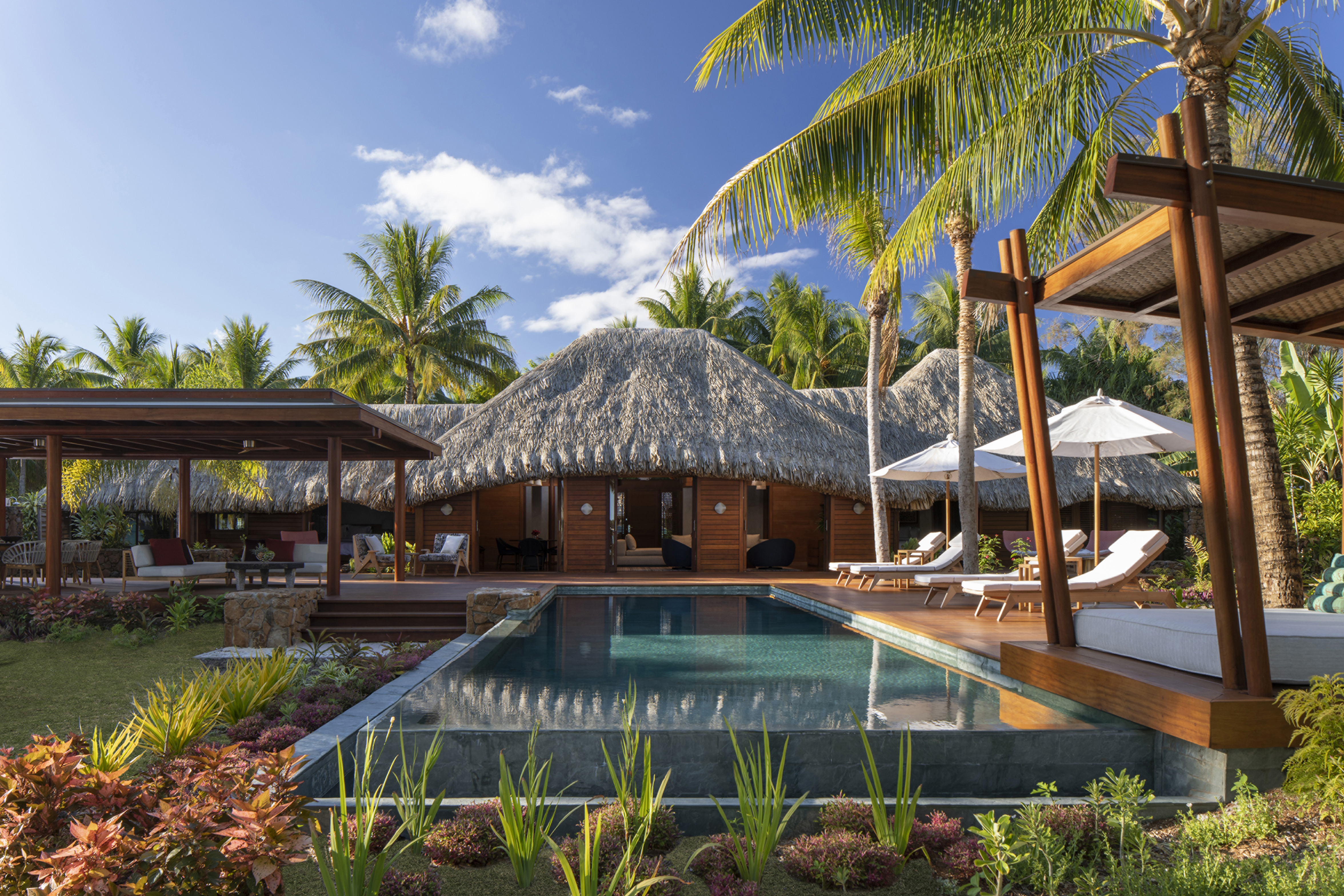 A wooden and thatch villa at Four Seasons Resort Bora Bora with a big pool and shaded cabanas surrounded by palms