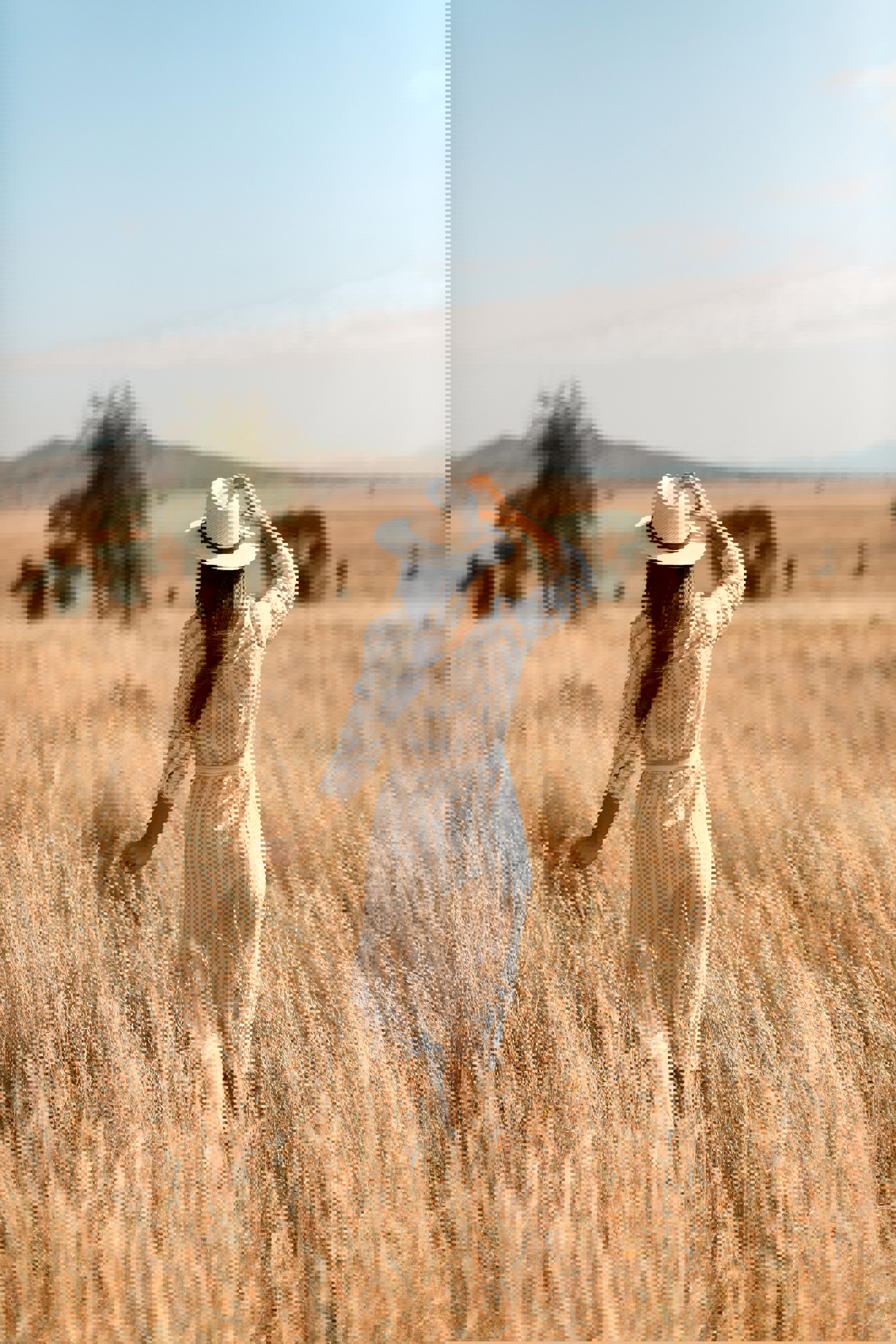 A woman wearing a dress and hat stood in long grass