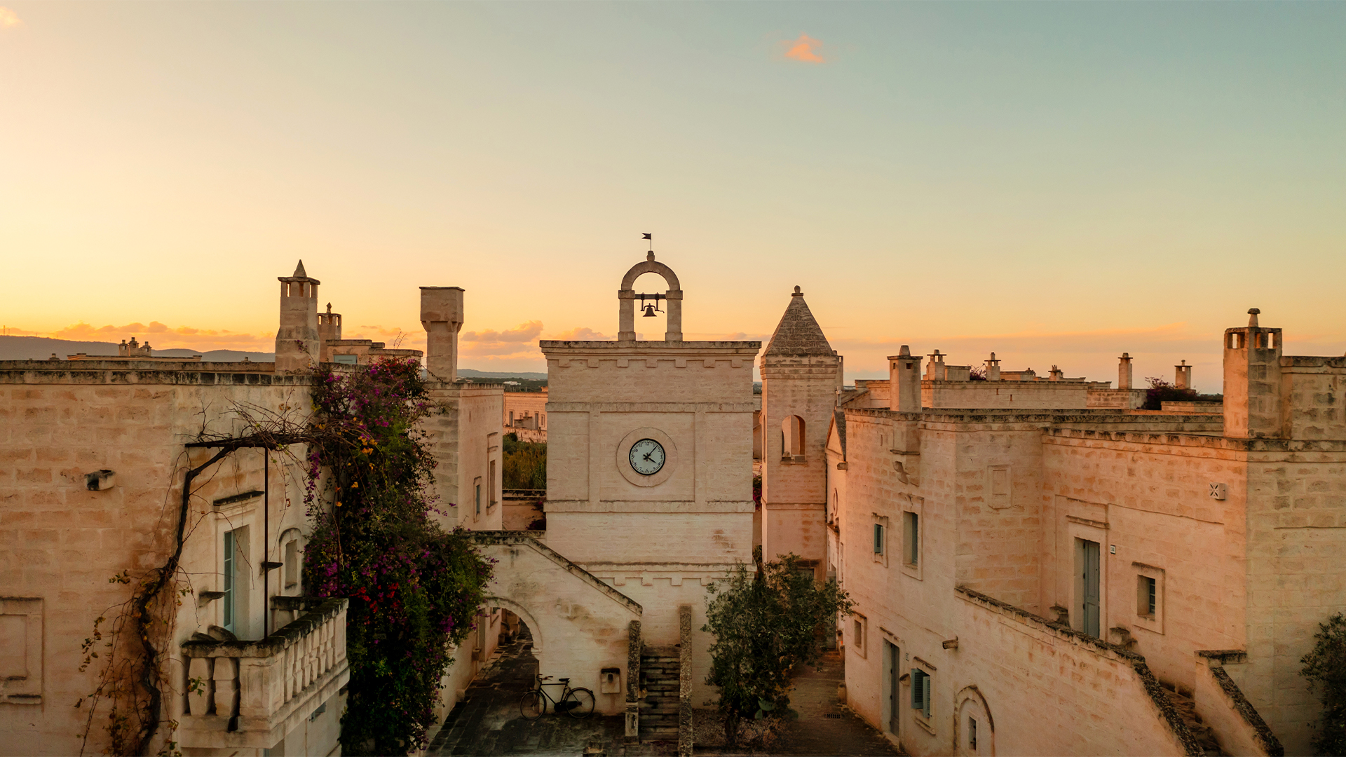 Sunset view over an ancient town with historic stone buildings and a clock tower under a clear sky.
