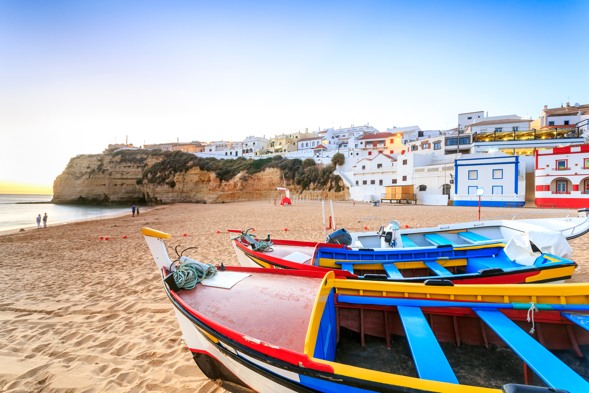 Two boats on a sandy beach next to white buildings in beach in Carvoeiro