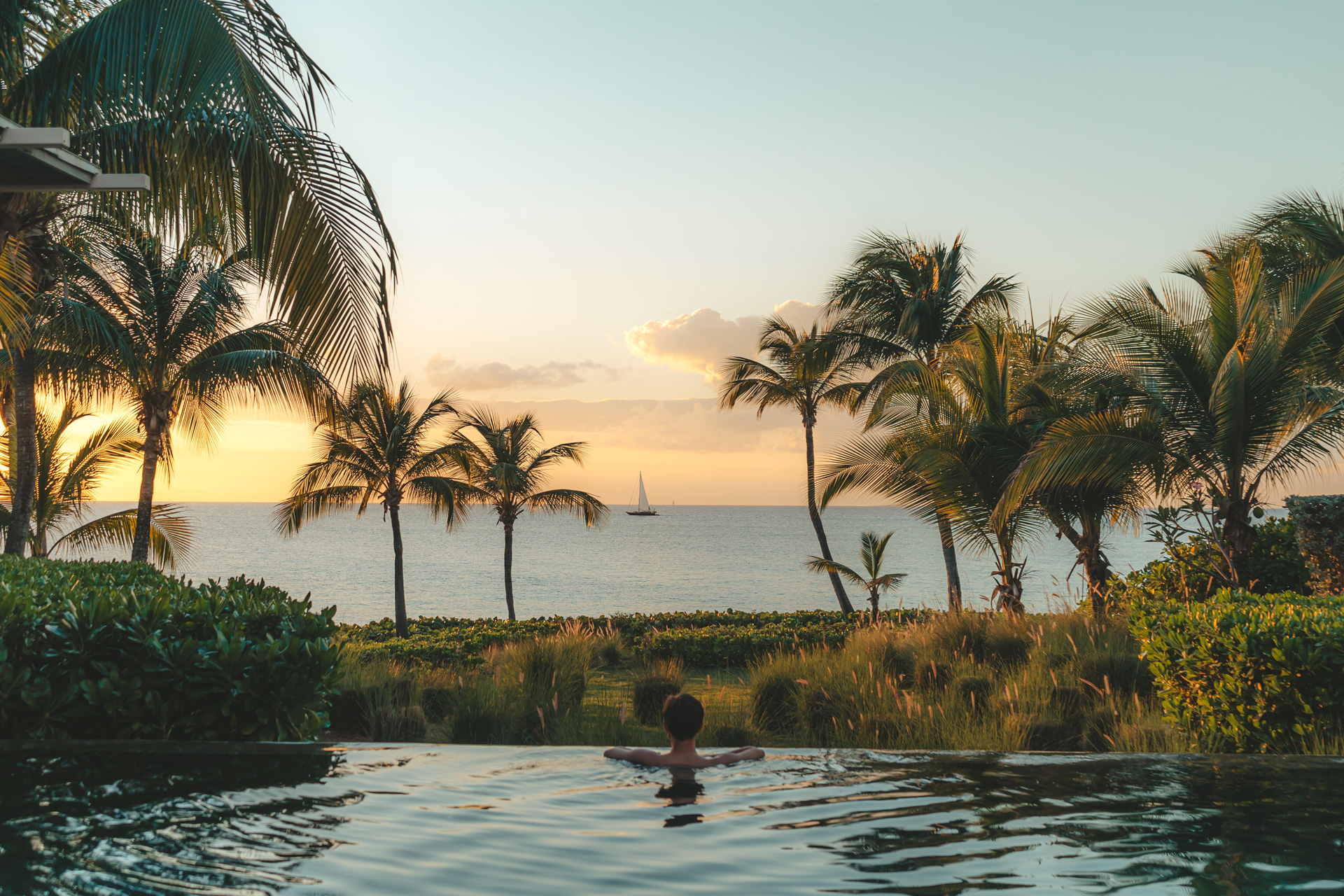 A person at the edge of an infinity pool looking out at a boat in the sea