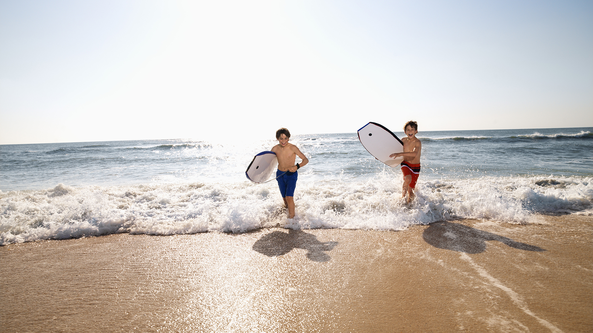 Two boys running up the beach from the sea with body boards