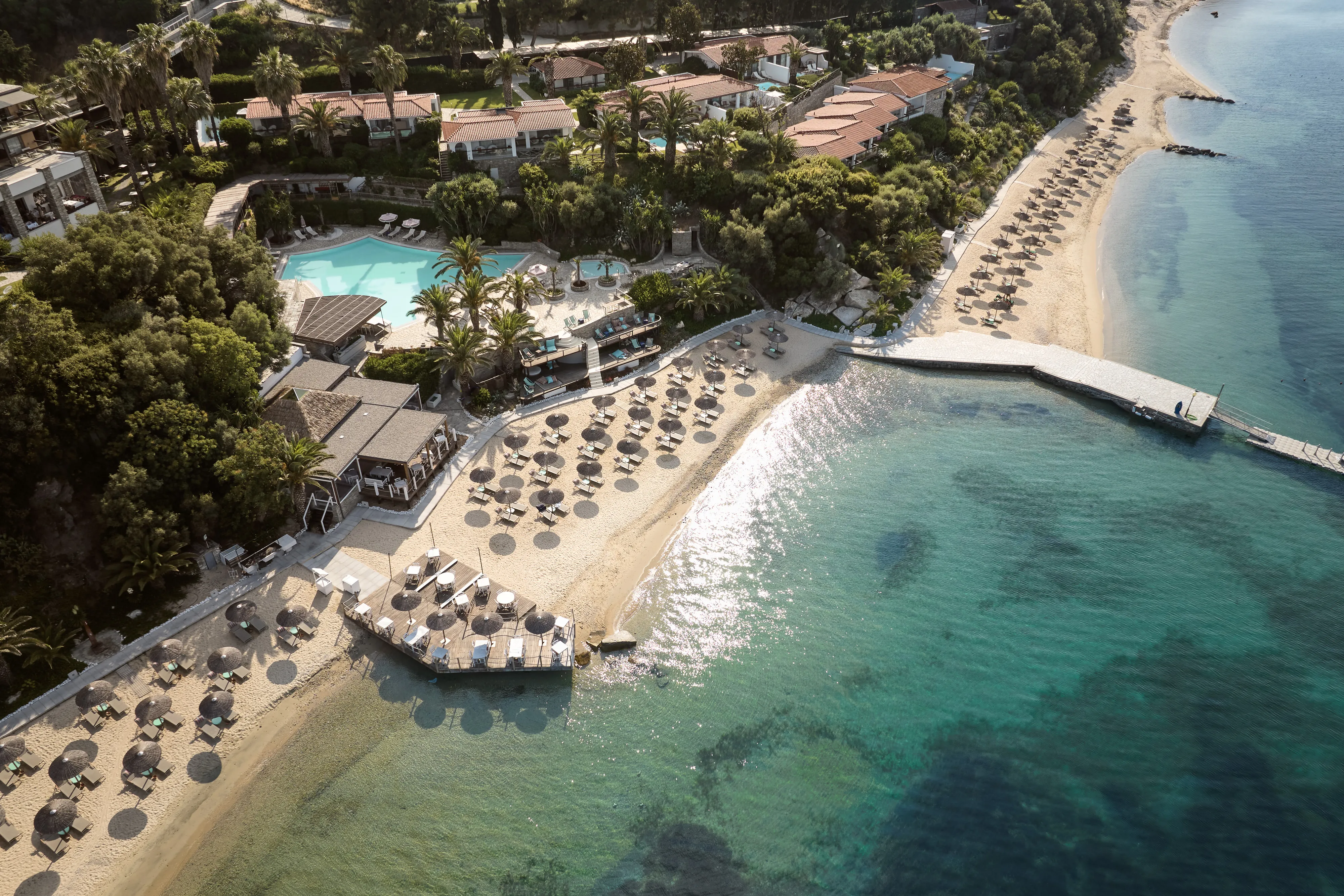 Aerial view of Eagles Palace in Greece showcasing its sandy beach, turquoise sea, sun loungers and resort pools surrounded by lush greenery.