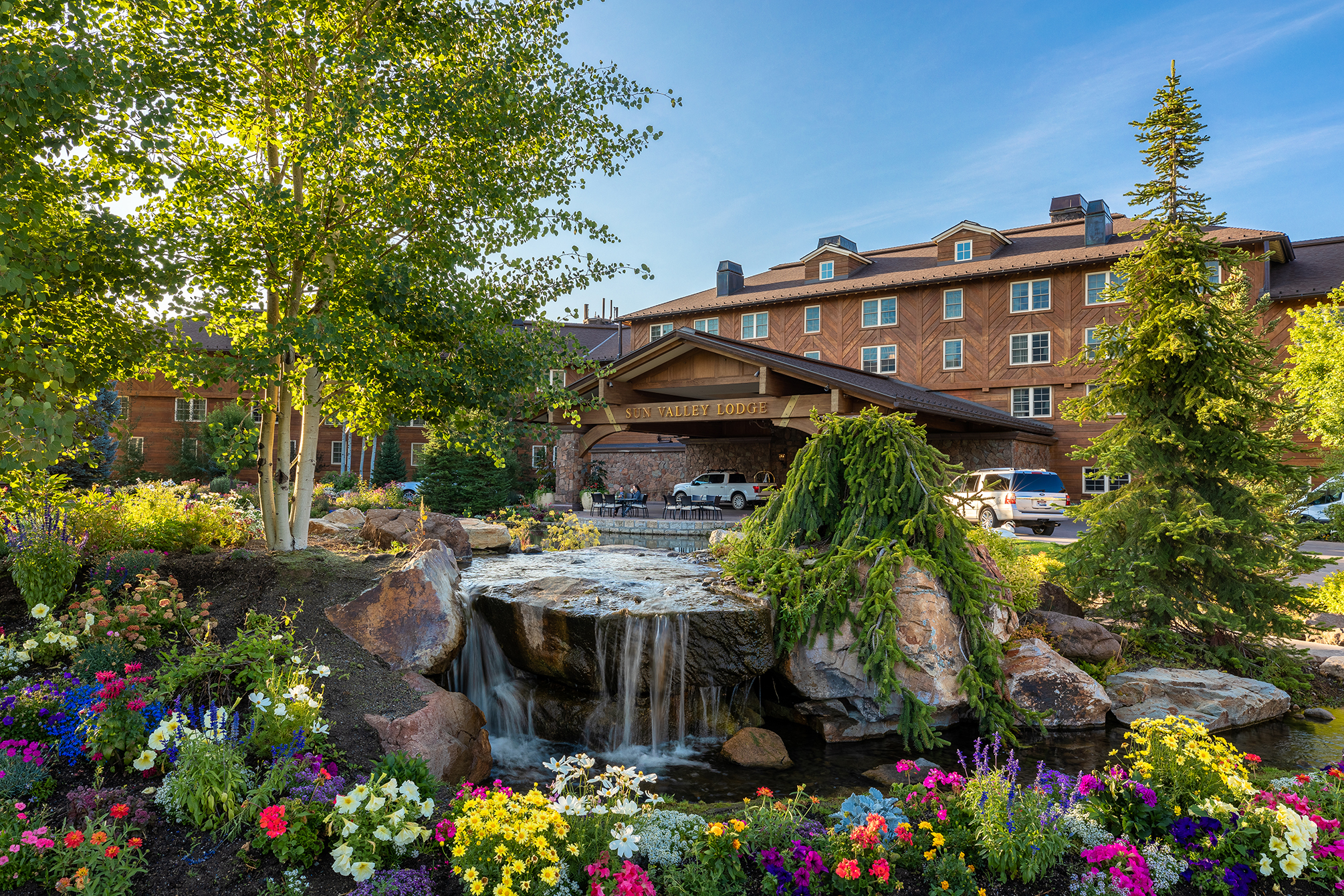 The exterior of Sun Valley Lodge with a beautiful garden featuring colourful flowers, a small waterfall, and lush greenery in the foreground