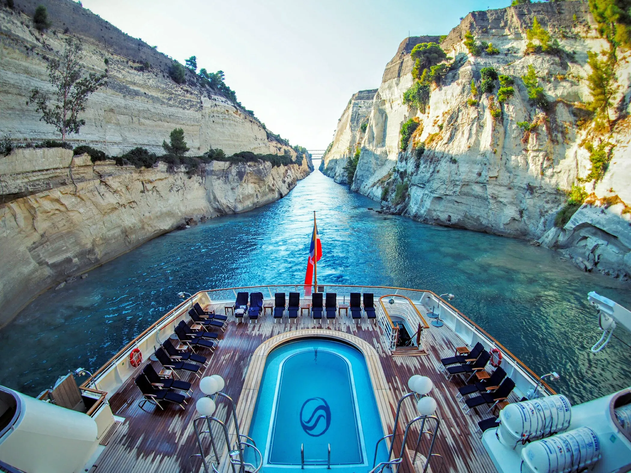 Luxury yacht with a pool cruising through a narrow canal between steep rocky cliffs.